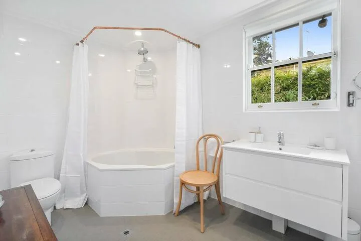 A bright bathroom with a bathtub, shower, sink, and window.