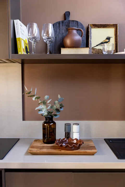 A kitchen counter sits beneath a shelf with glassware and decorative items.