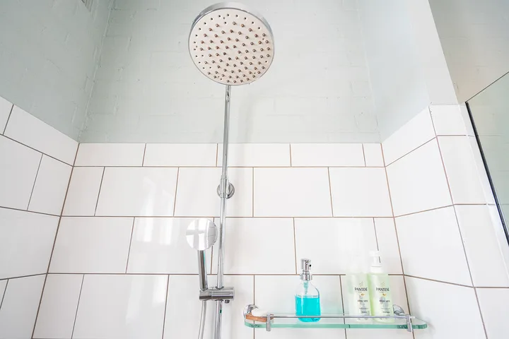 A tiled shower area with a large overhead showerhead and glass shelf.