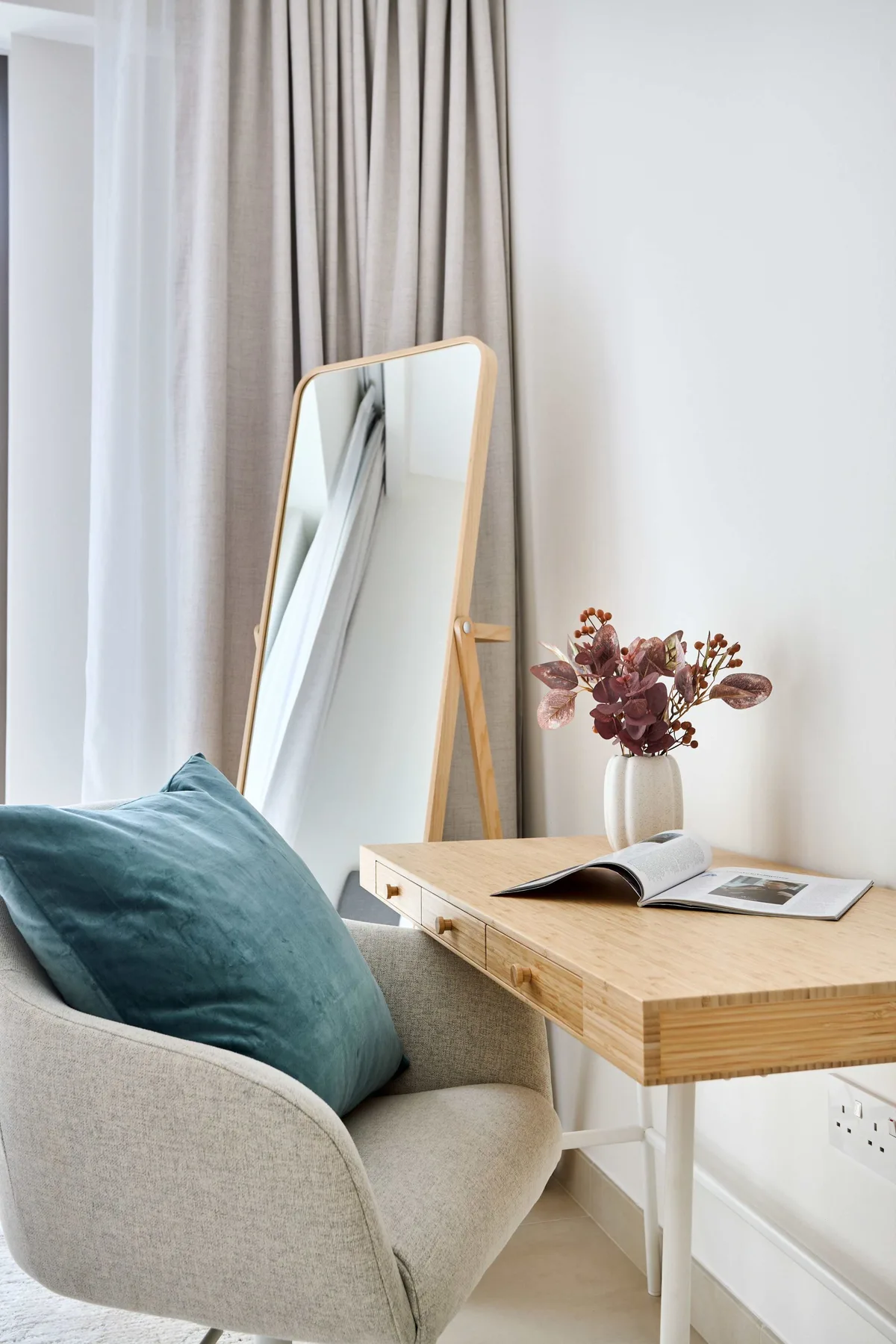 A small writing desk sits beside a cushioned chair and a standing mirror.
