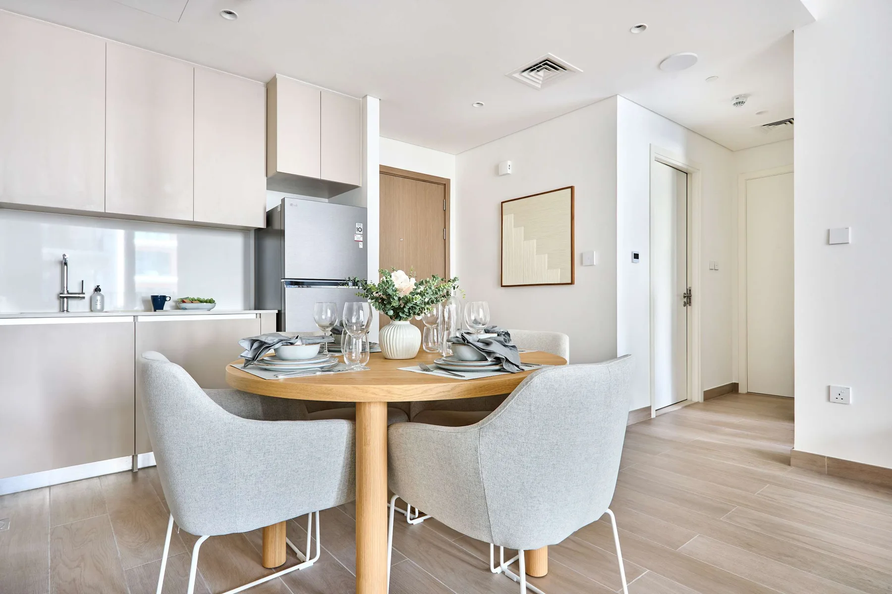 A bright dining area has a round table set beside a white kitchen.
