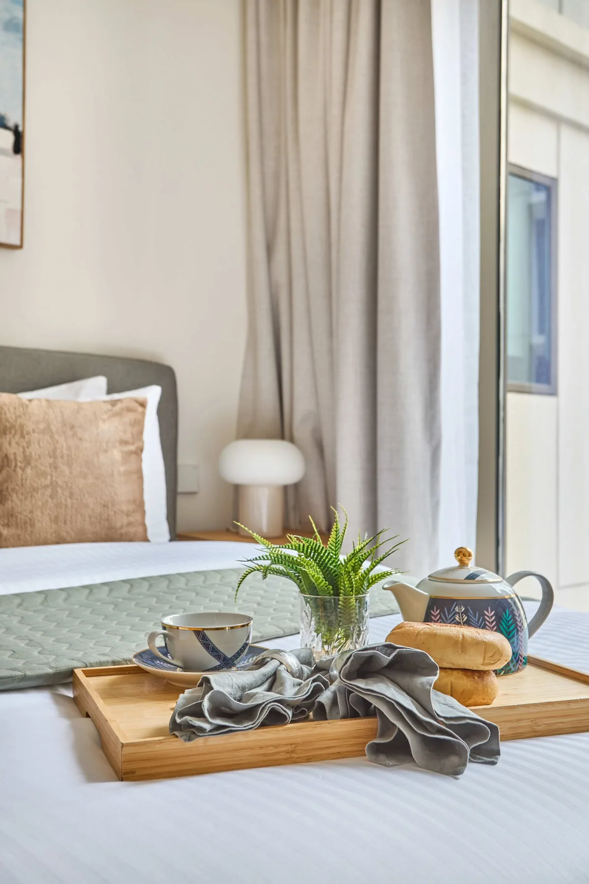 A bedroom scene with a bed and a breakfast tray holding tea and a plant.