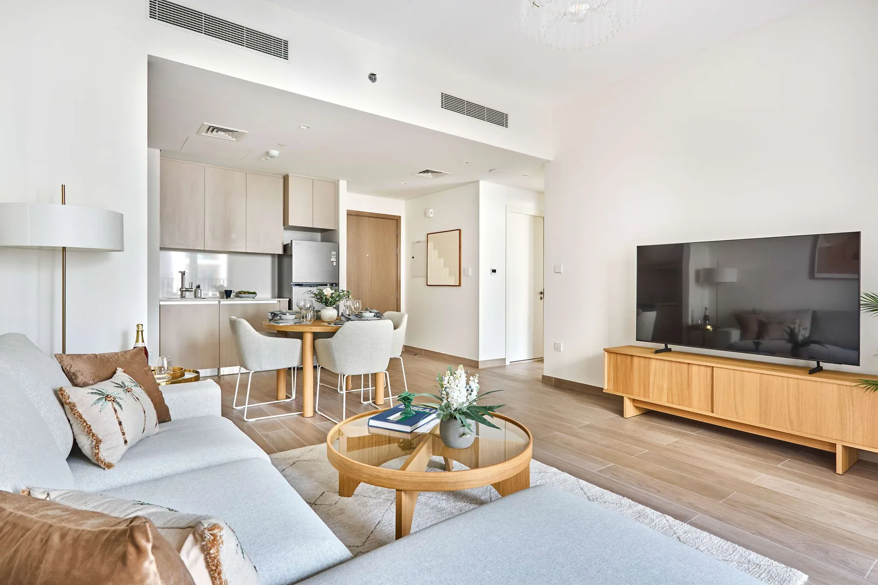 A bright living room with seating, a television, and an open kitchen-dining area.