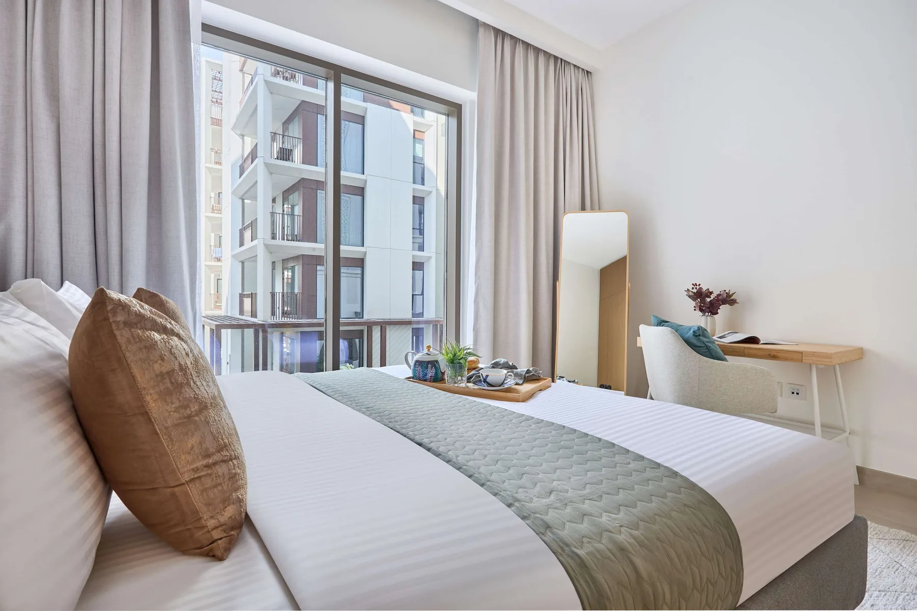 A bright bedroom with a large bed beside a window overlooking nearby buildings.