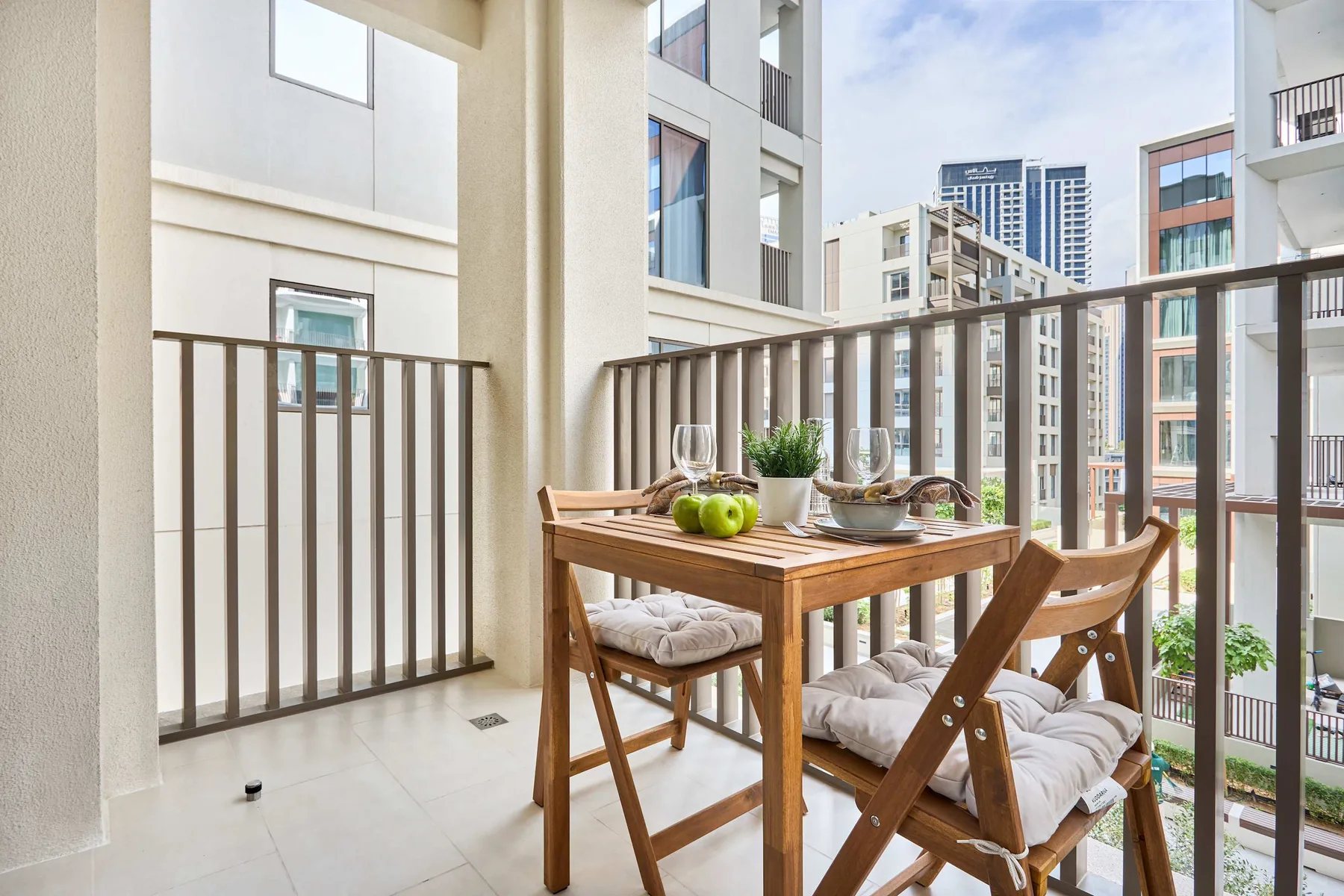 A balcony dining area with a wooden table and cushioned chairs overlooks nearby buildings.