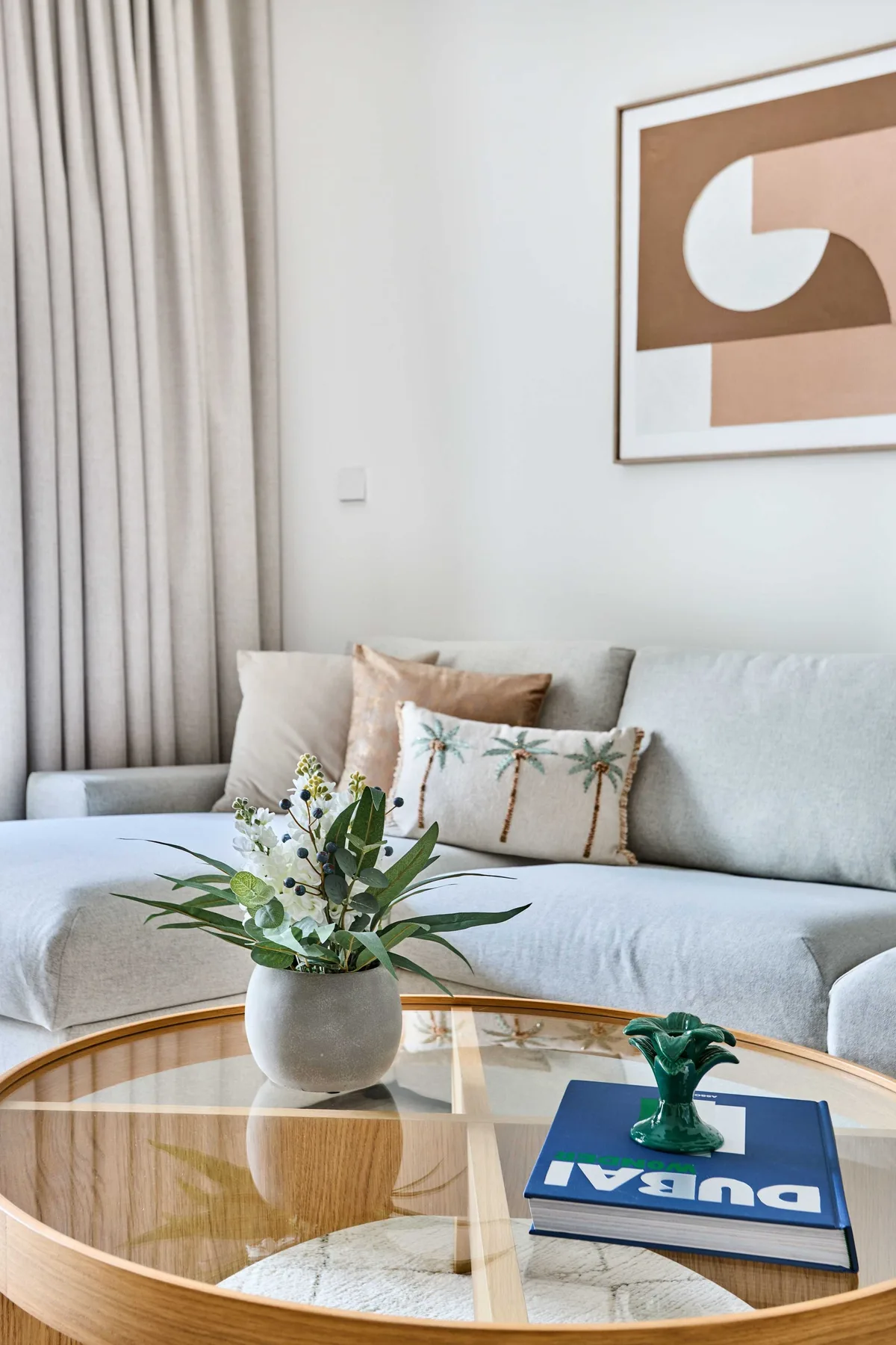 A bright living room with light seating, a glass coffee table, and framed abstract art.