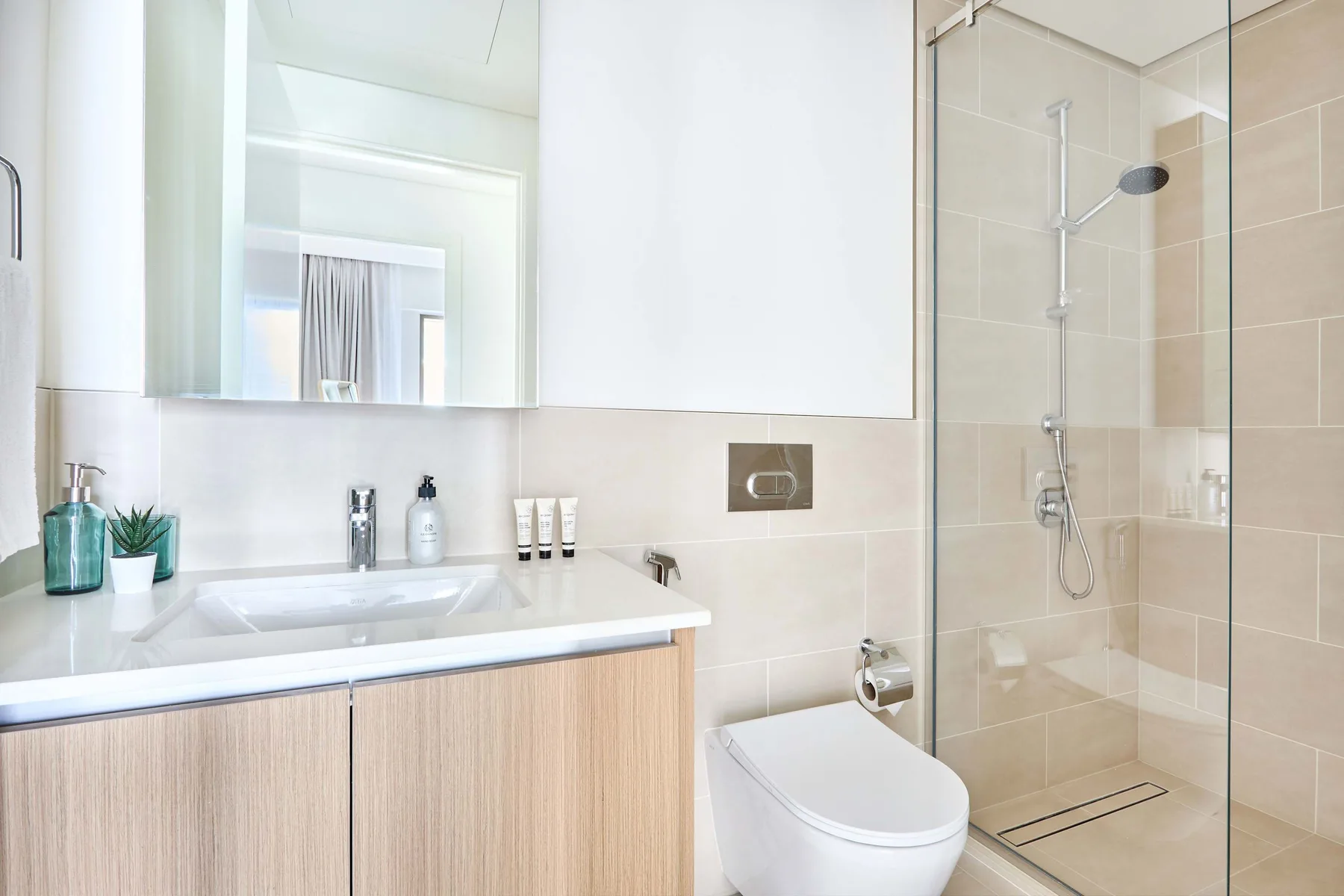 A bright bathroom with a vanity, sink, toilet, and glass shower.