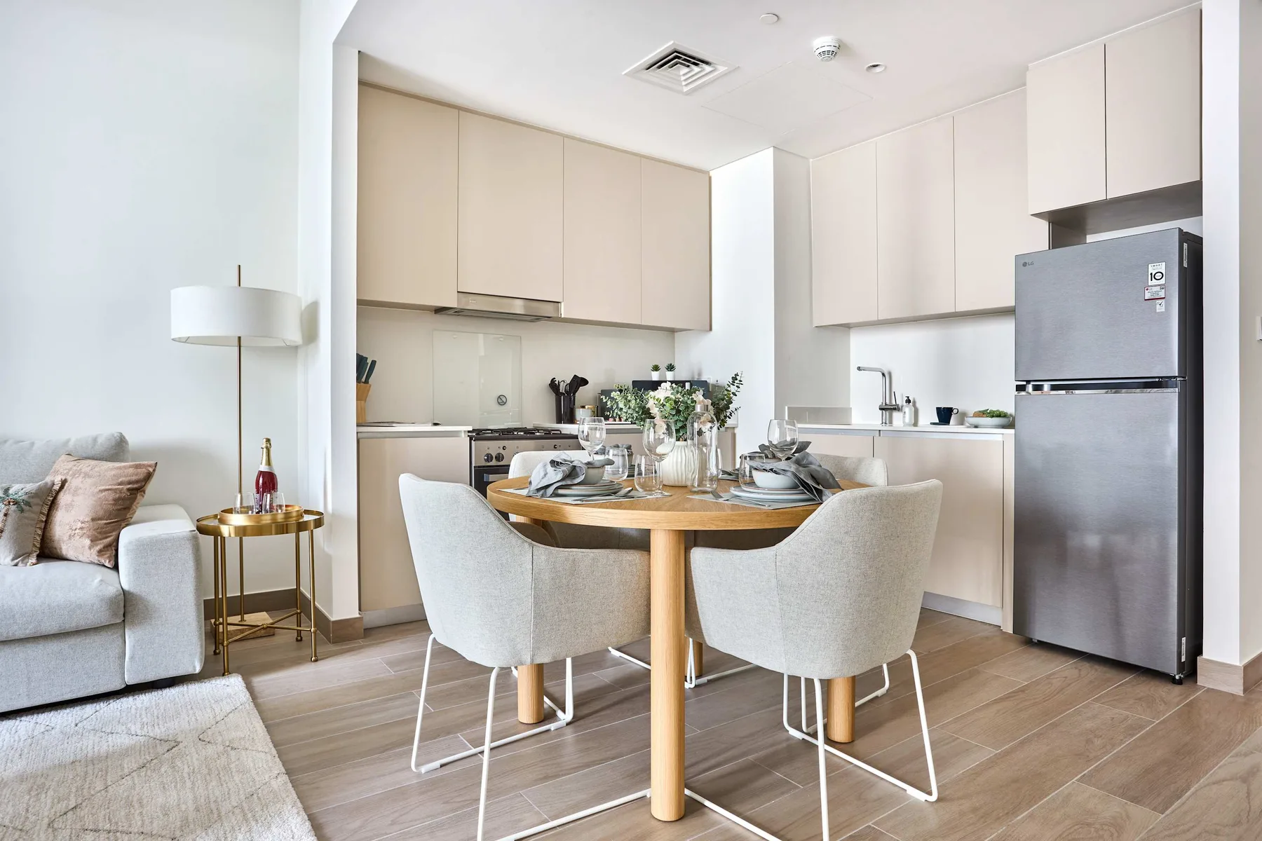 A bright dining area opens onto a modern kitchen, with a set table and nearby seating.