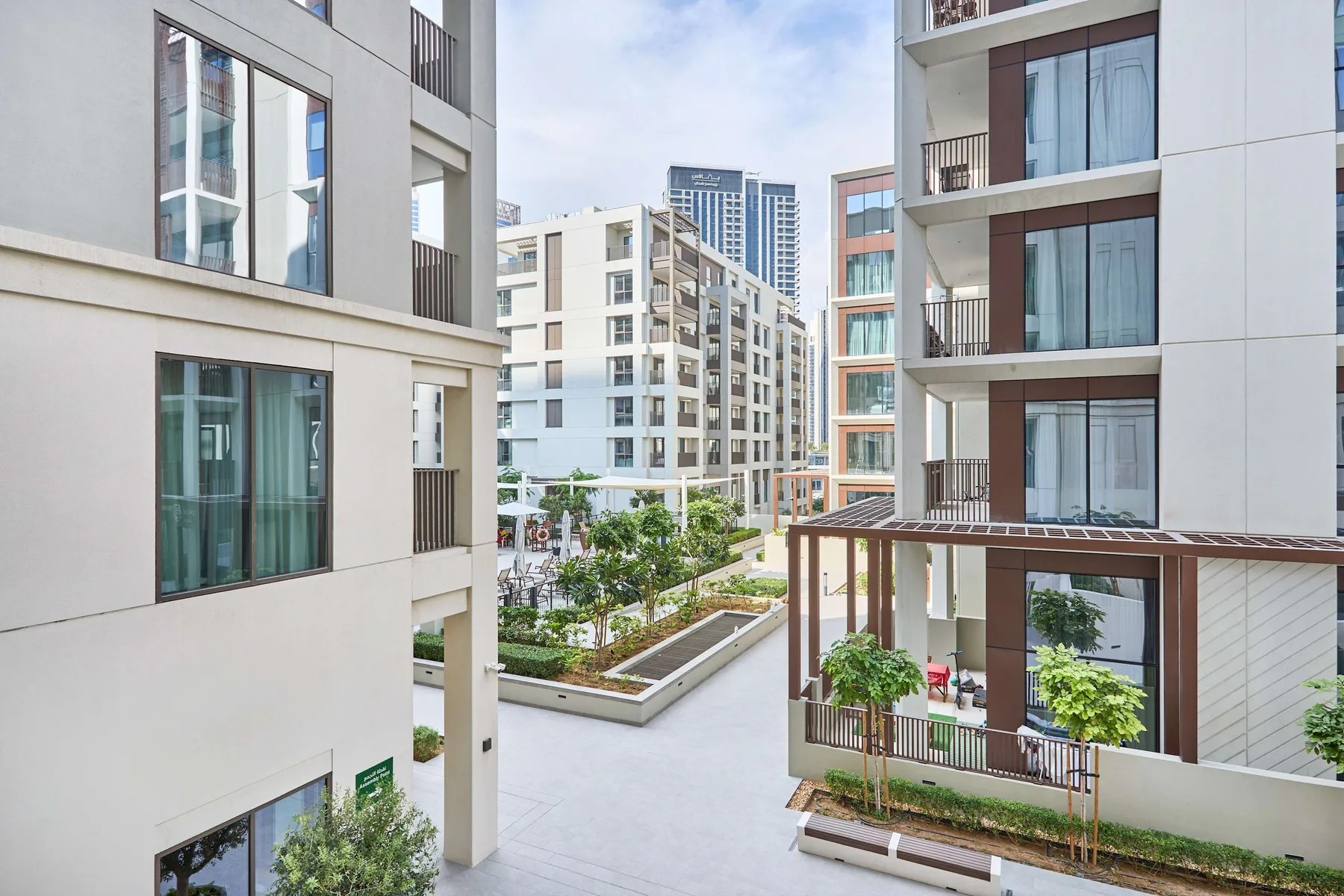 Modern apartment buildings surround a landscaped courtyard with trees and paved walkways.