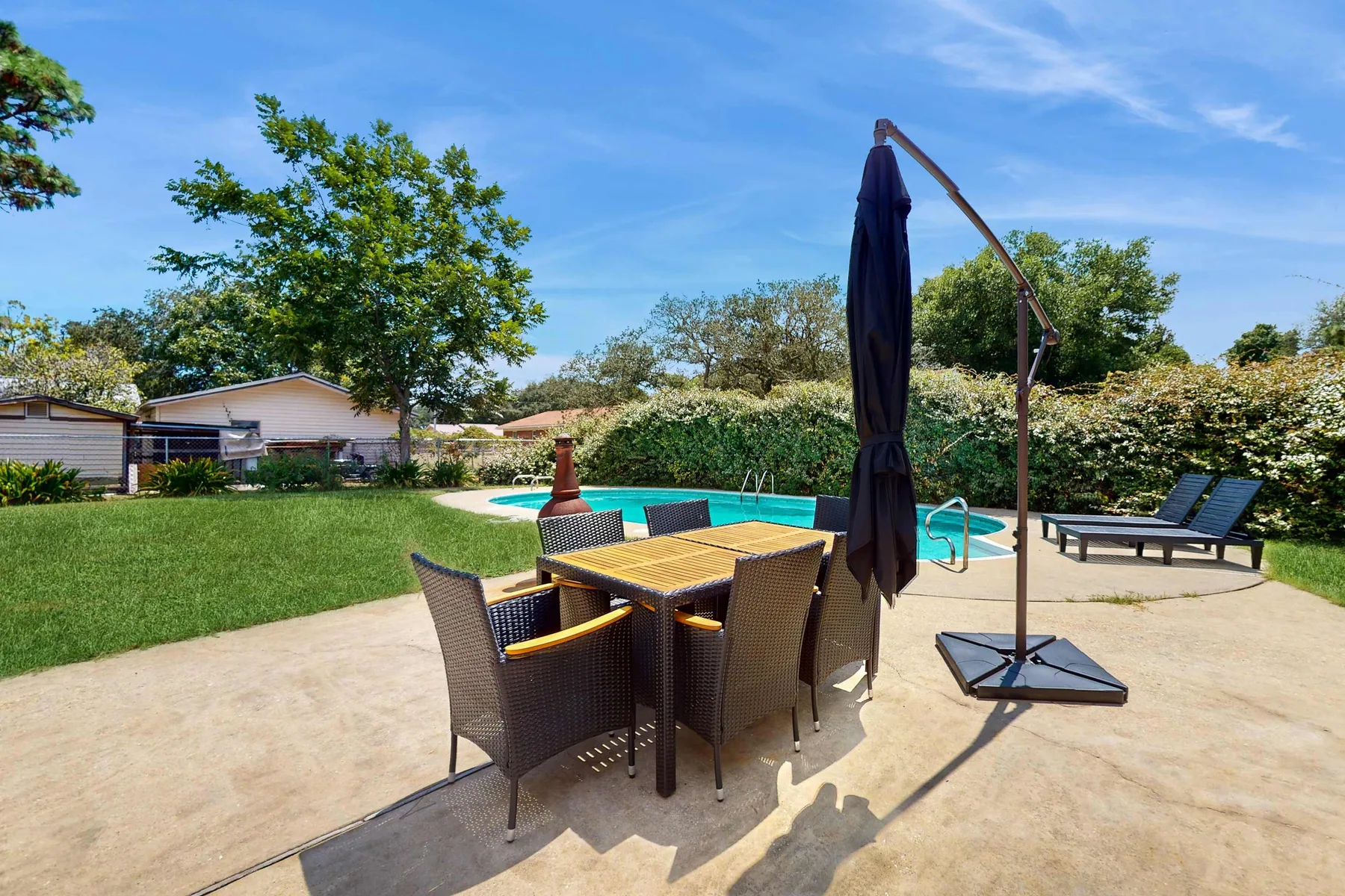 An outdoor patio with dining seating beside a swimming pool and lawn.