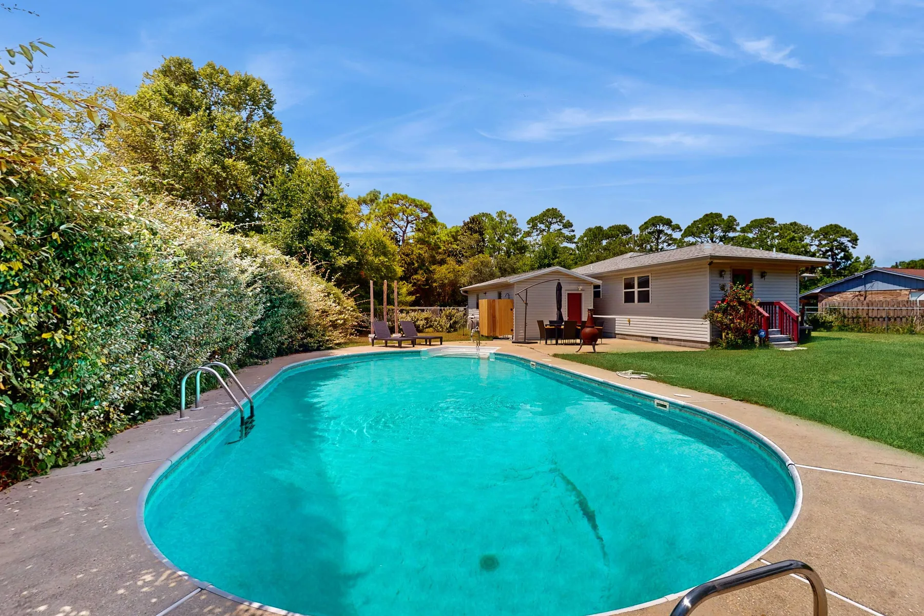 Una piscina al aire libre está junto a una casa de una planta y un césped verde.