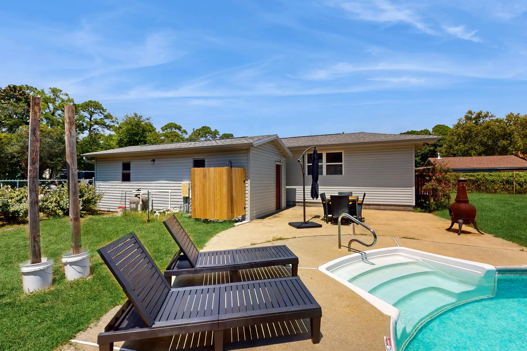 A backyard patio features lounge seating beside a small swimming pool.