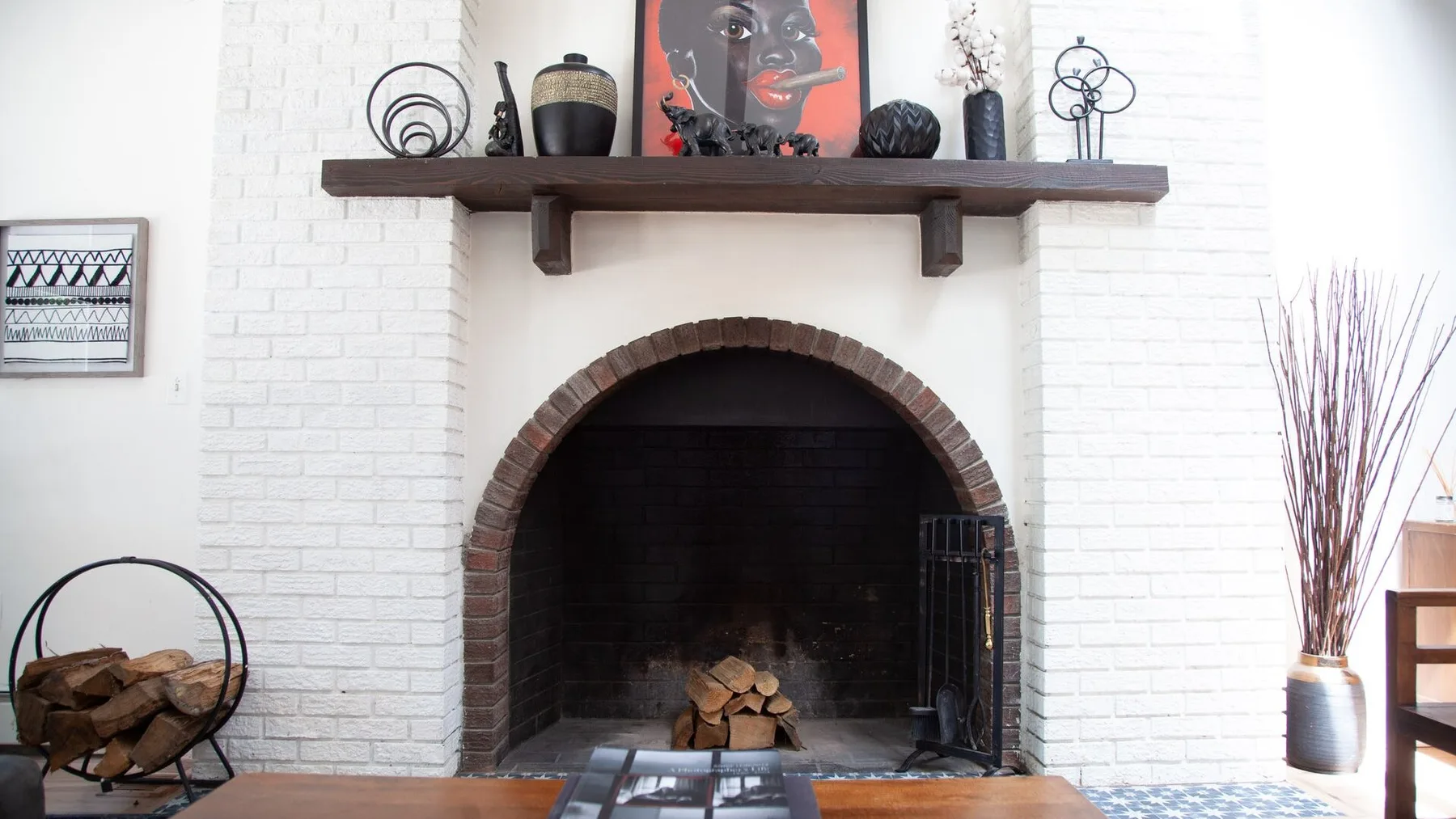 Una chimenea de ladrillo blanco con repisa oscura y objetos decorativos.