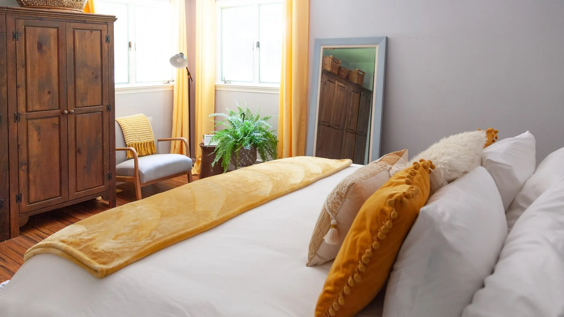 Un dormitorio luminoso con una cama tendida, un armario de madera y ventanas.