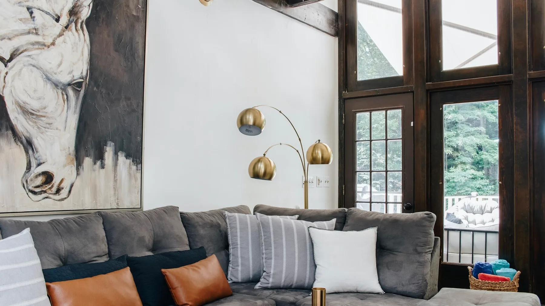 Una sala de estar con un sofá gris, arte en la pared y ventanas altas.