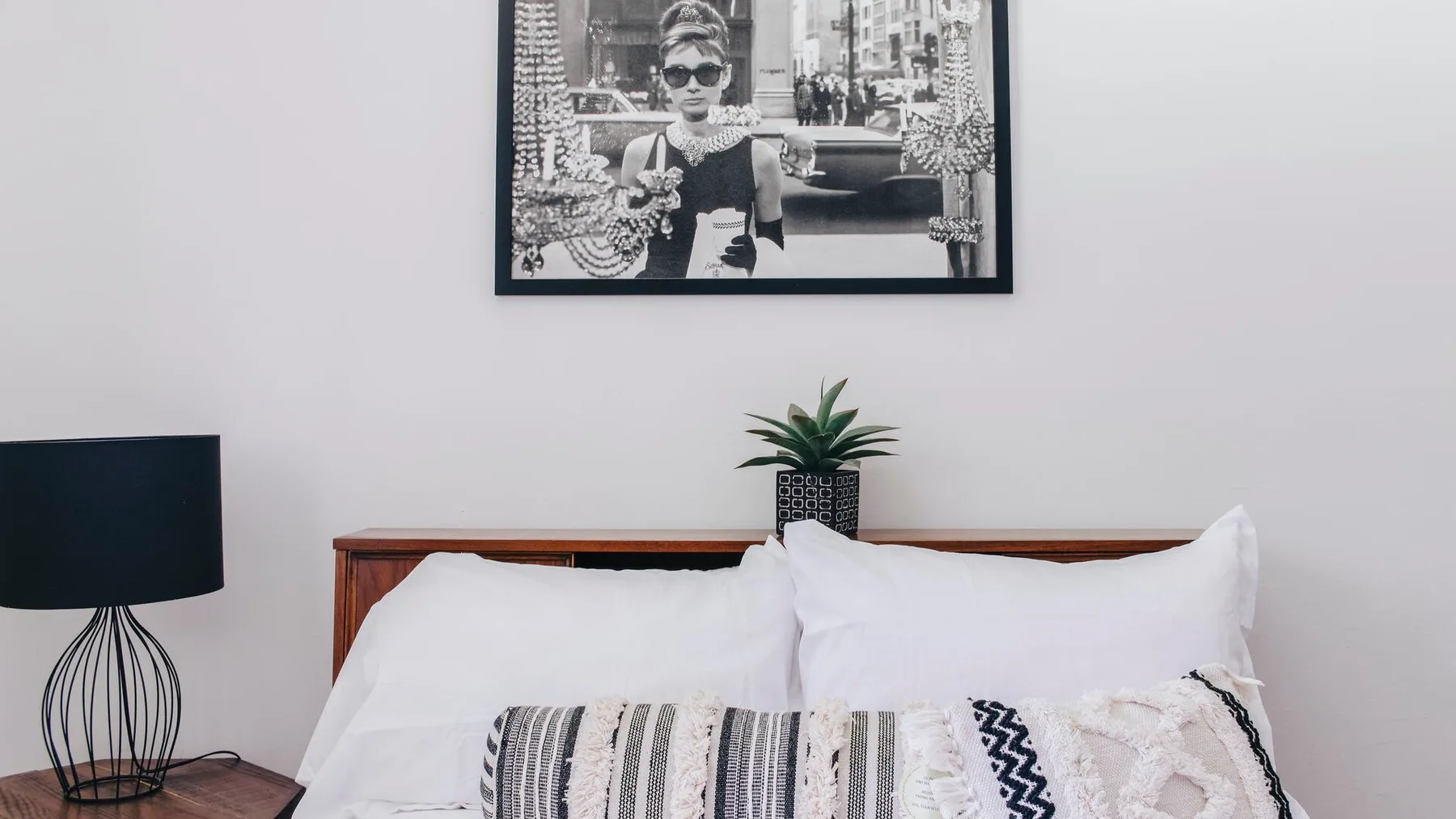 Un dormitorio con una cama de madera, ropa de cama blanca y un cuadro enmarcado.