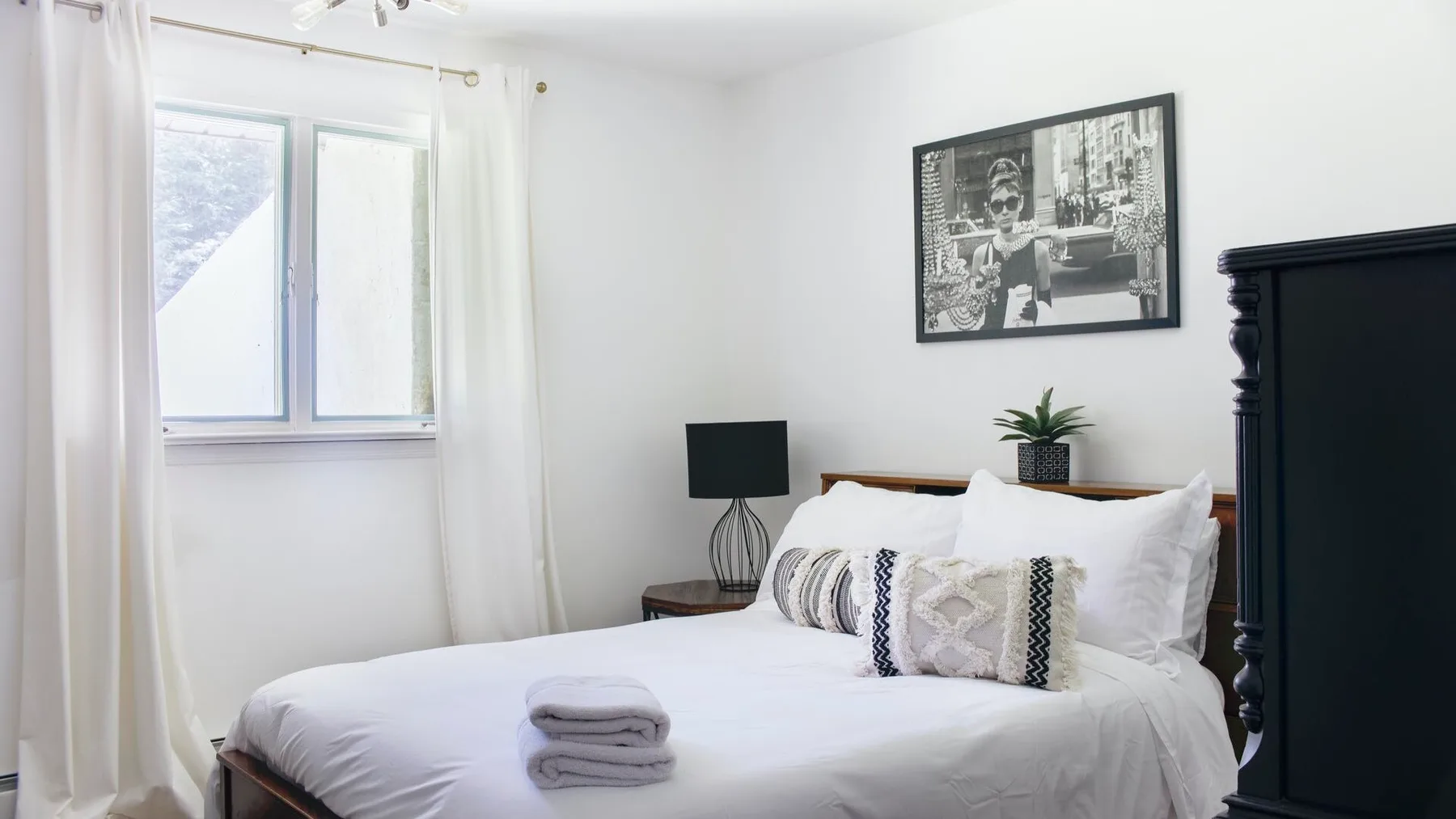Un dormitorio luminoso con una cama bien hecha y una ventana enmarcada por cortinas.