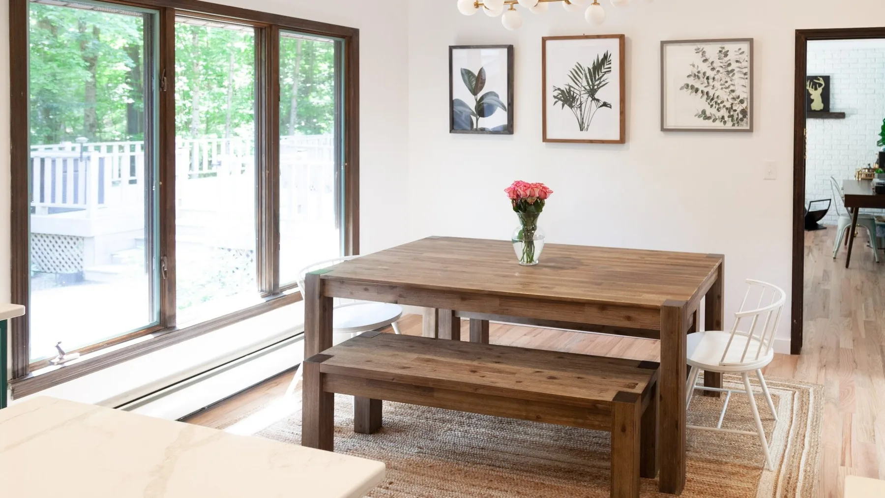 Comedor con una mesa y un banco de madera junto a grandes ventanas.