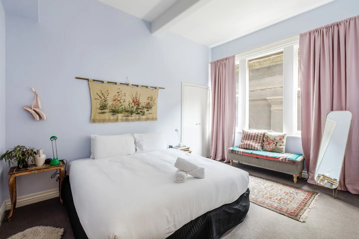 A bedroom with a neatly made bed and a cushioned window seat framed by pink curtains.