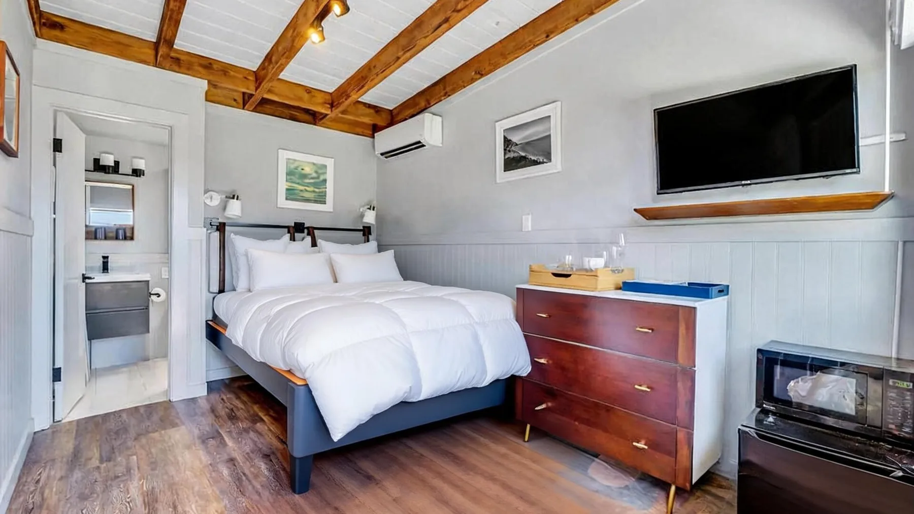 A bedroom with a bed, wooden ceiling beams, and a wall-mounted television.