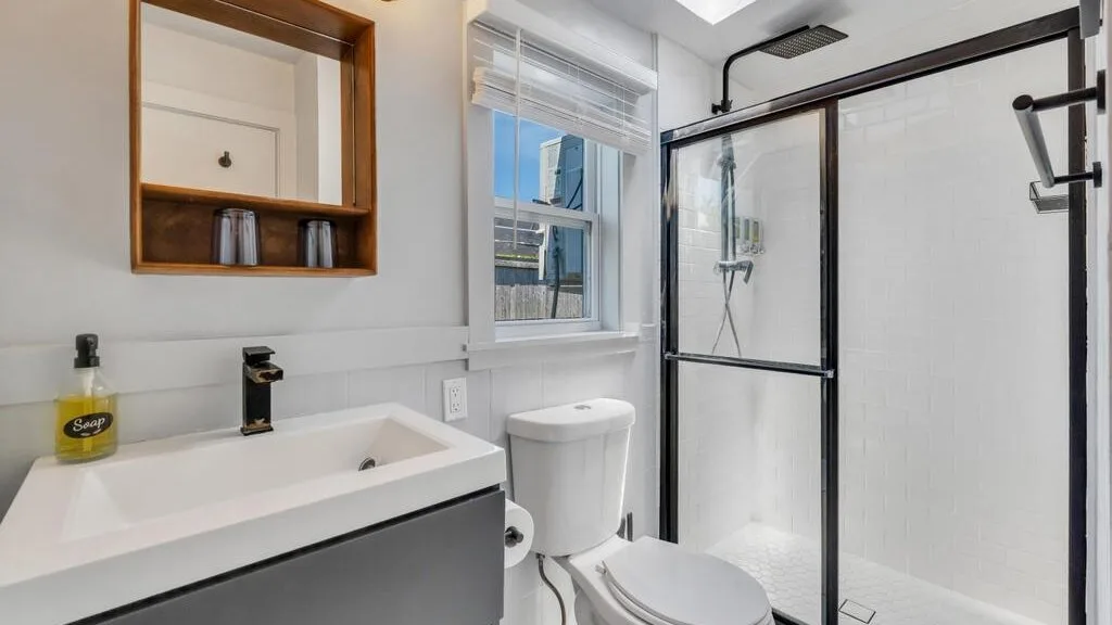 A bright bathroom with a sink, window, and glass shower.