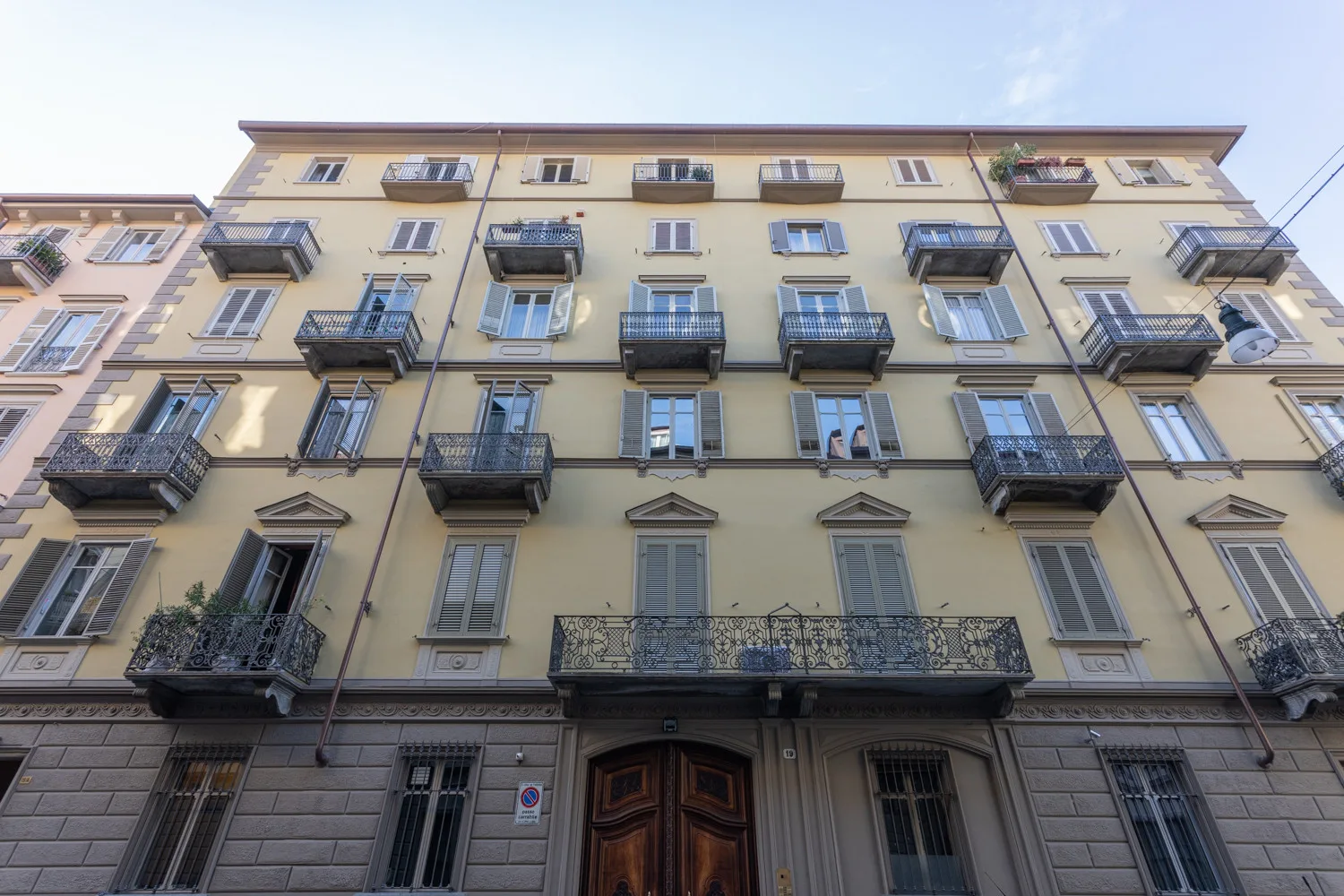 Fachada de un edificio claro de varios pisos con balcones y una gran entrada de madera.