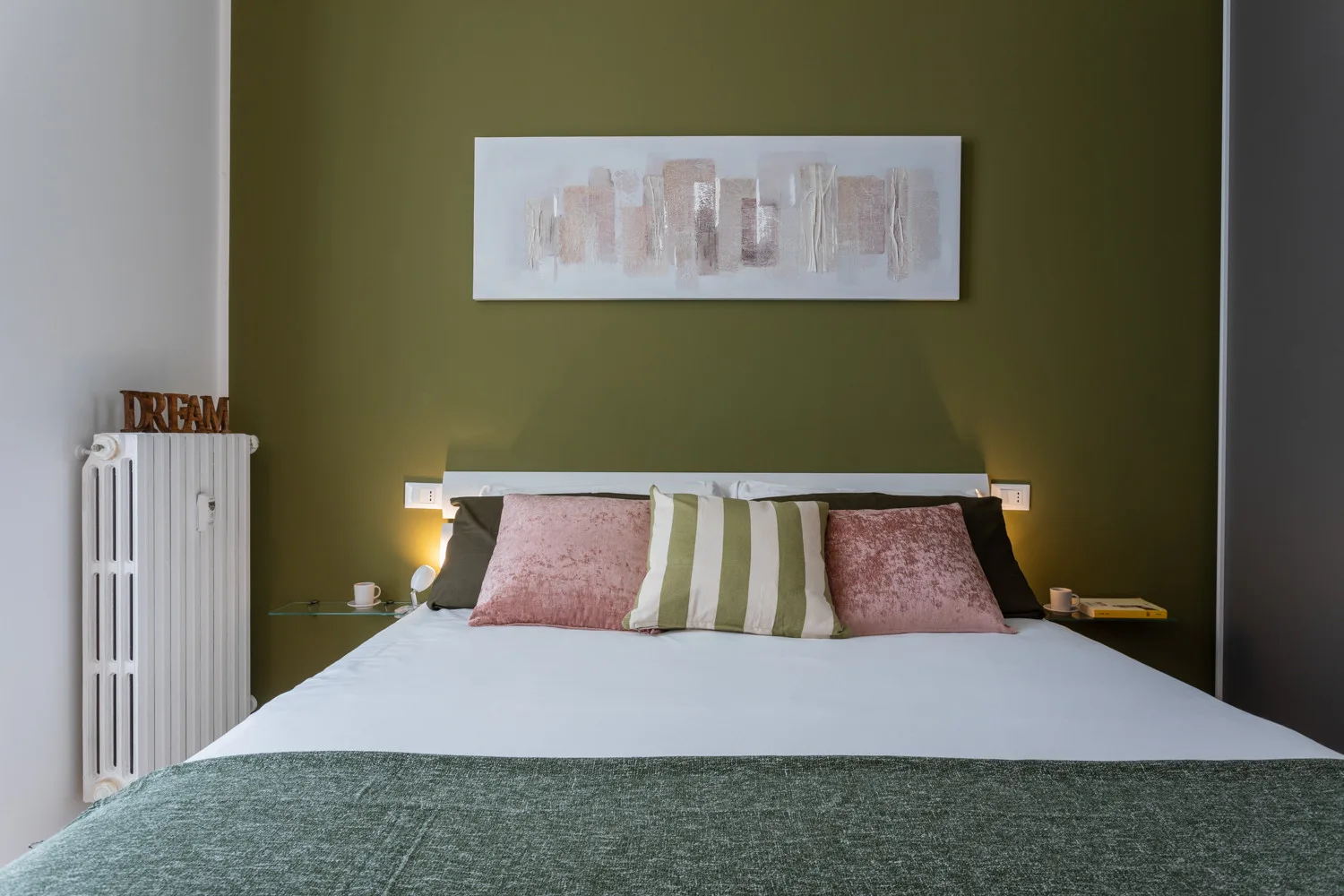 Un dormitorio con una cama y almohadas frente a una pared verde oliva.