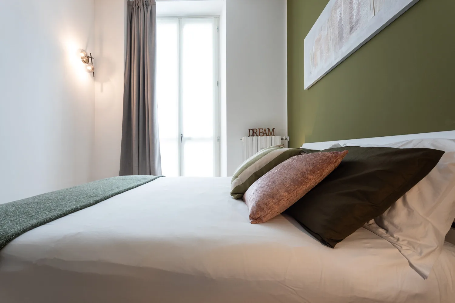 Un dormitorio con una cama bien hecha y almohadas junto a una ventana luminosa.