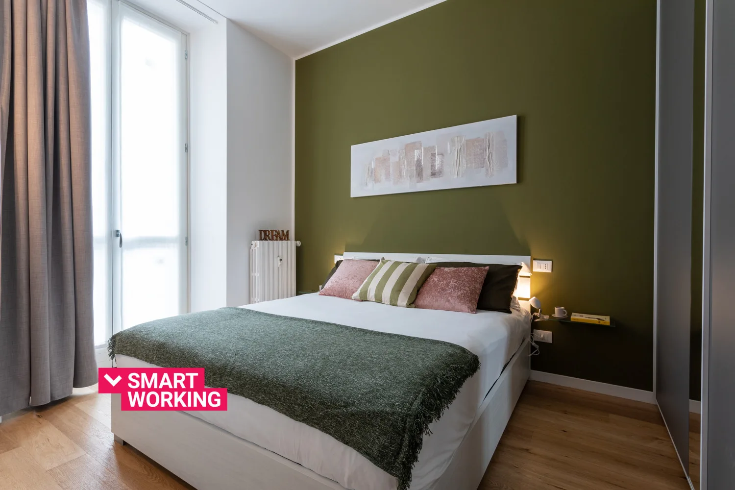 Un dormitorio con una cama junto a una pared verde oliva y una ventana alta.