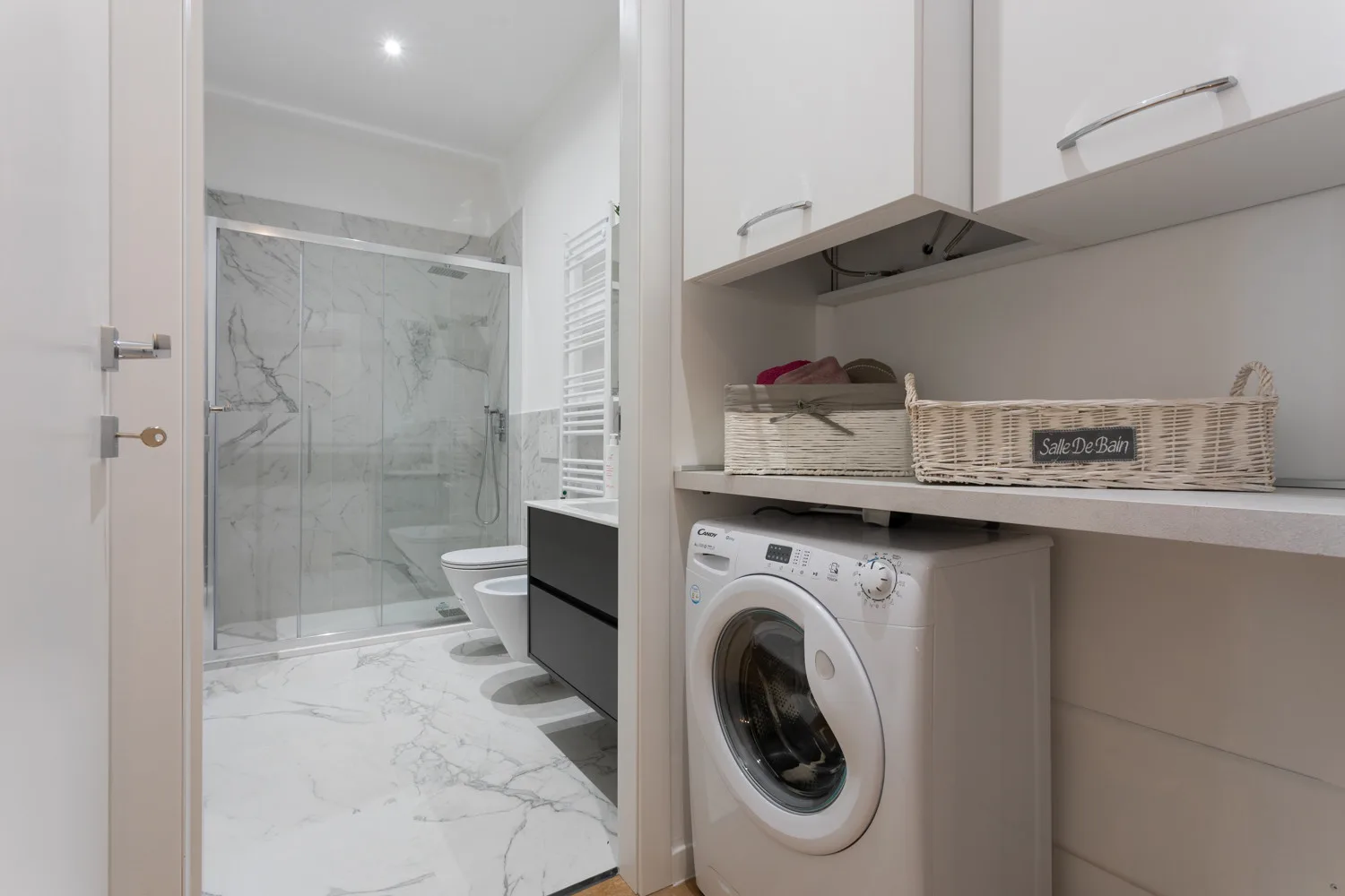 Baño con ducha de vidrio y lavadora en la zona de lavandería contigua.