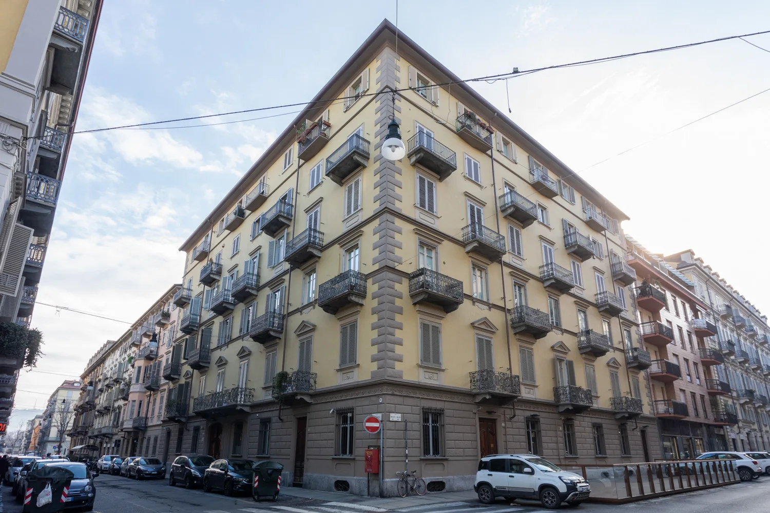 Un edificio amarillo de varias plantas con balcones da a una calle urbana.