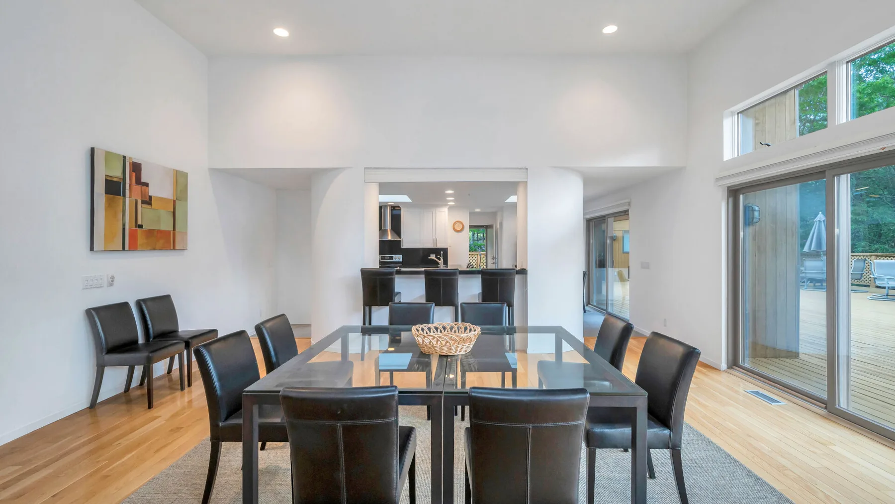 Un comedor luminoso con una mesa de vidrio y asientos oscuros junto a grandes ventanas.