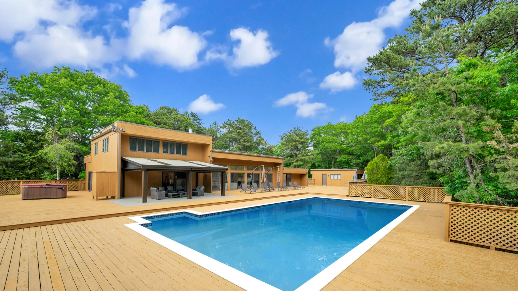Una casa moderna da a una terraza de madera con piscina.