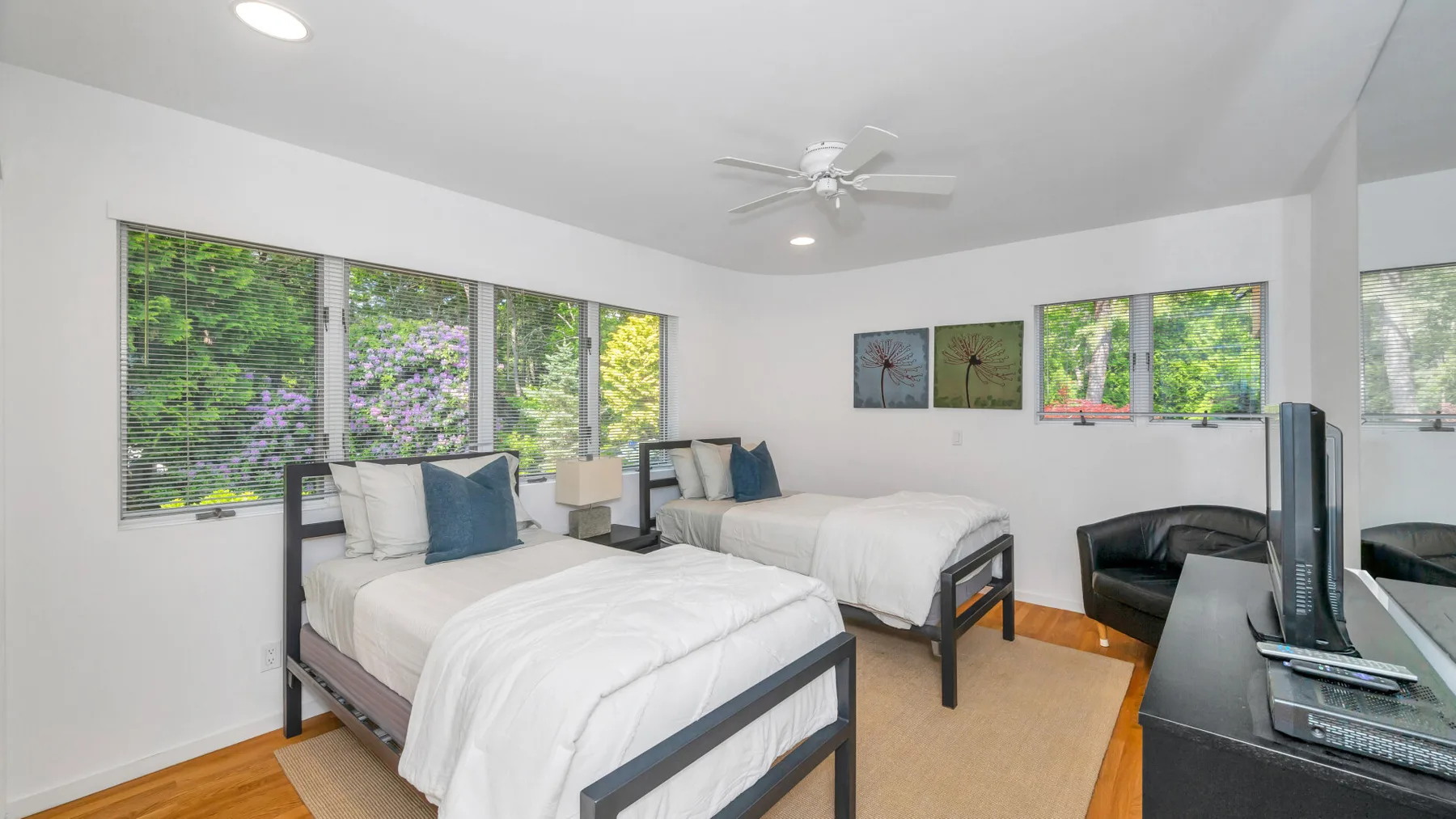 Un dormitorio luminoso con dos camas, ventanas grandes y un escritorio.