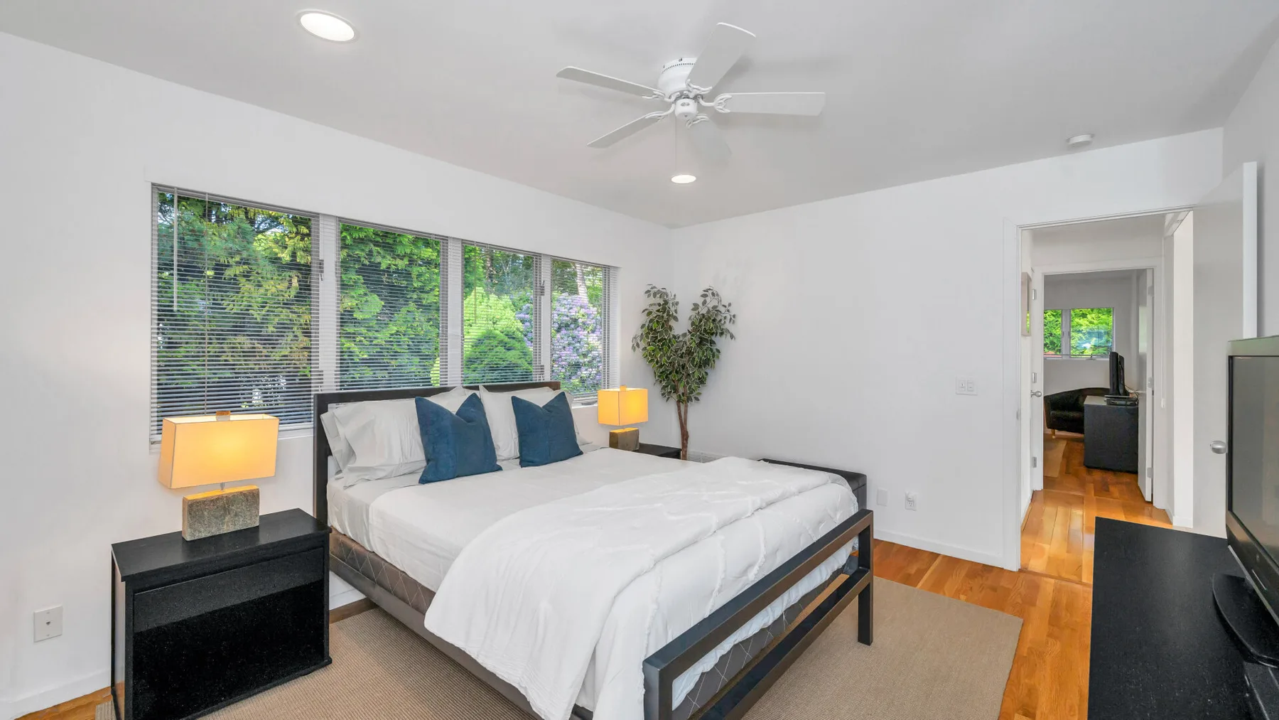 Un dormitorio luminoso con una cama grande junto a ventanas con vistas a la vegetación.