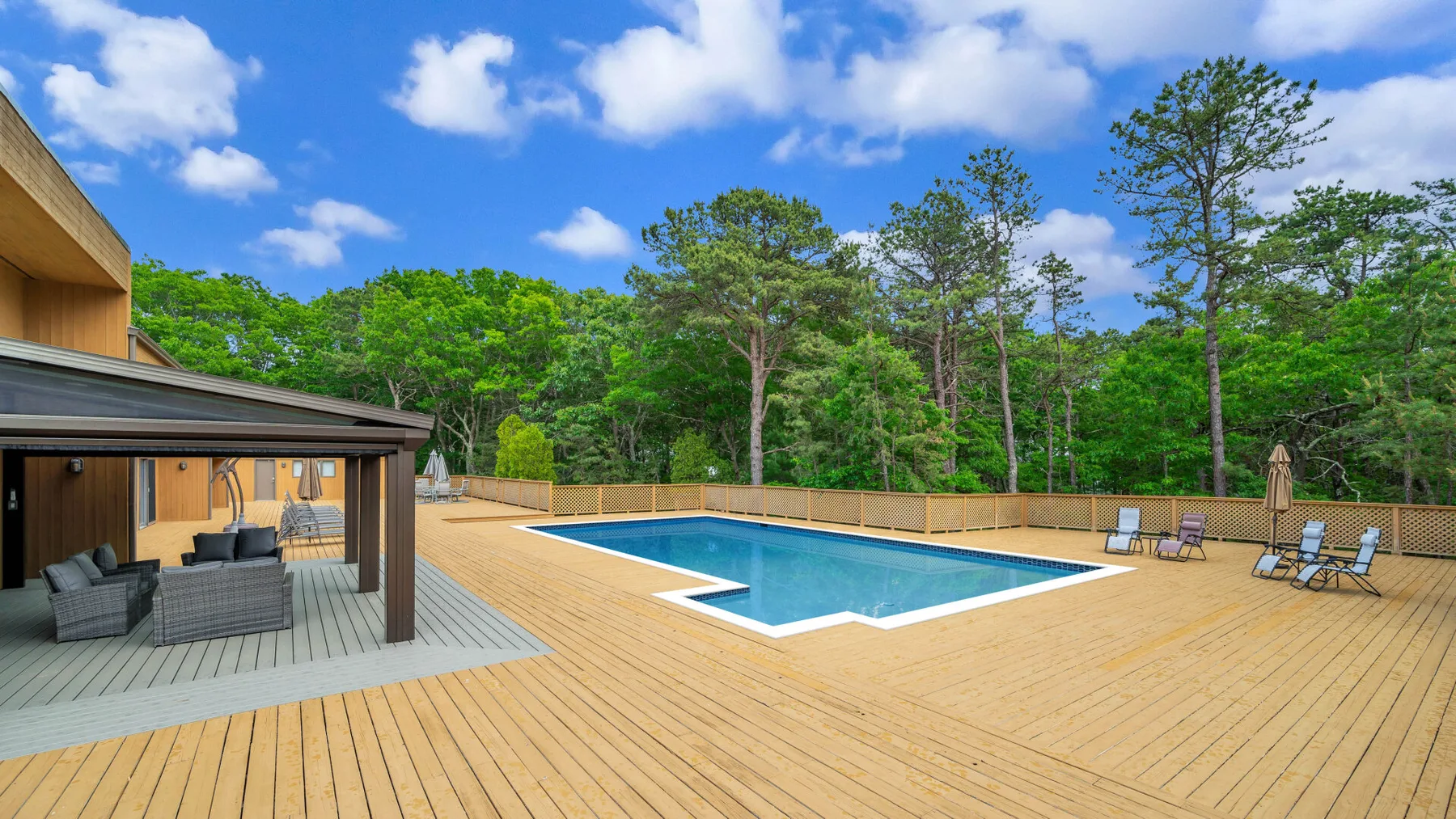 Una piscina está junto a una amplia terraza de madera y una zona de estar cubierta.