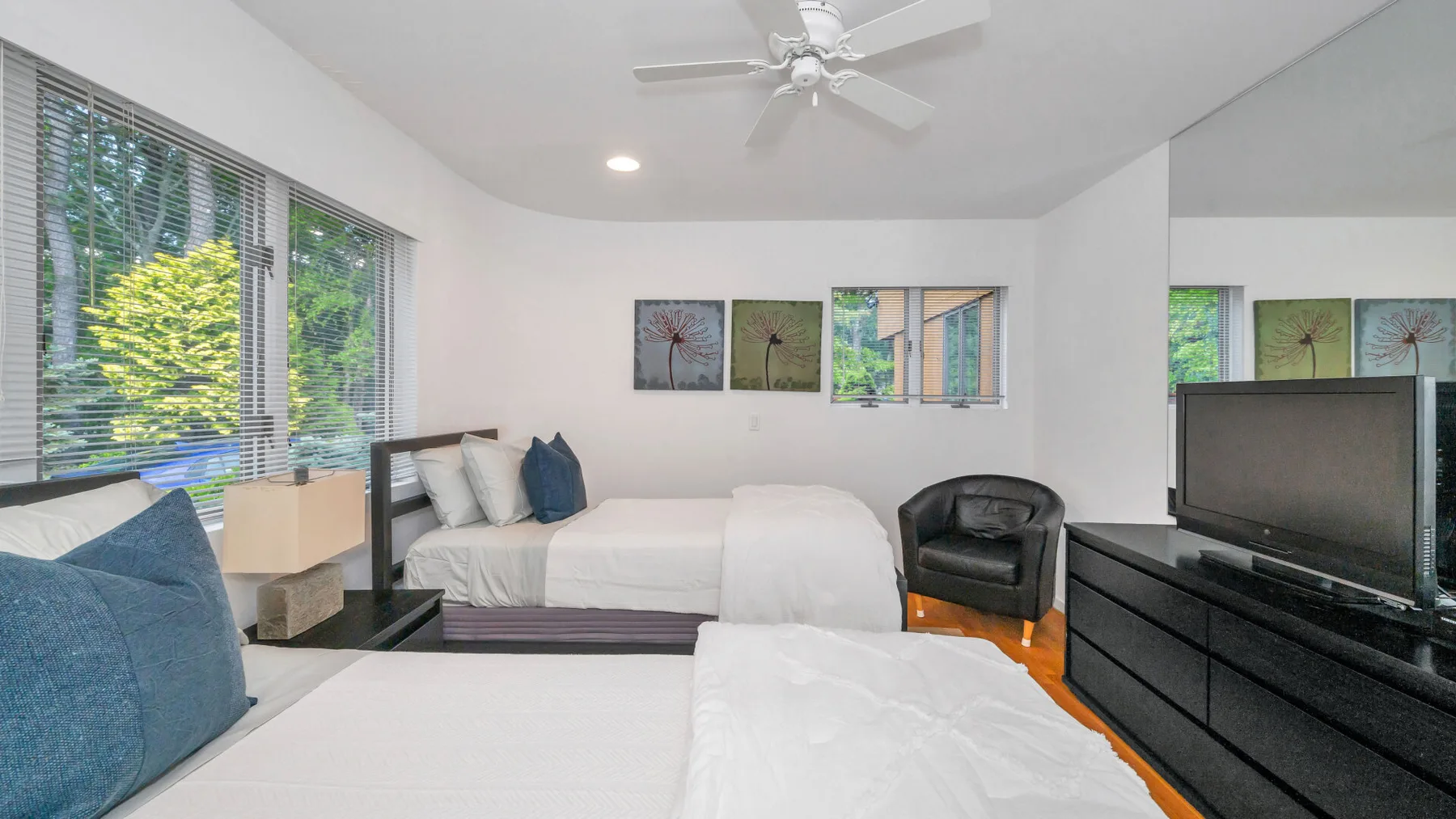Un dormitorio luminoso con ropa de cama blanca, grandes ventanas y un televisor.