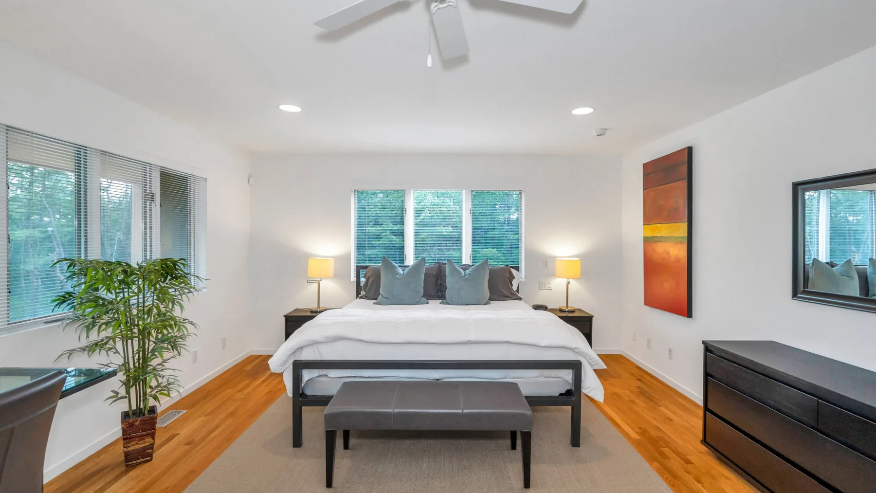 Un dormitorio luminoso con una cama, un banco y ventanas amplias.