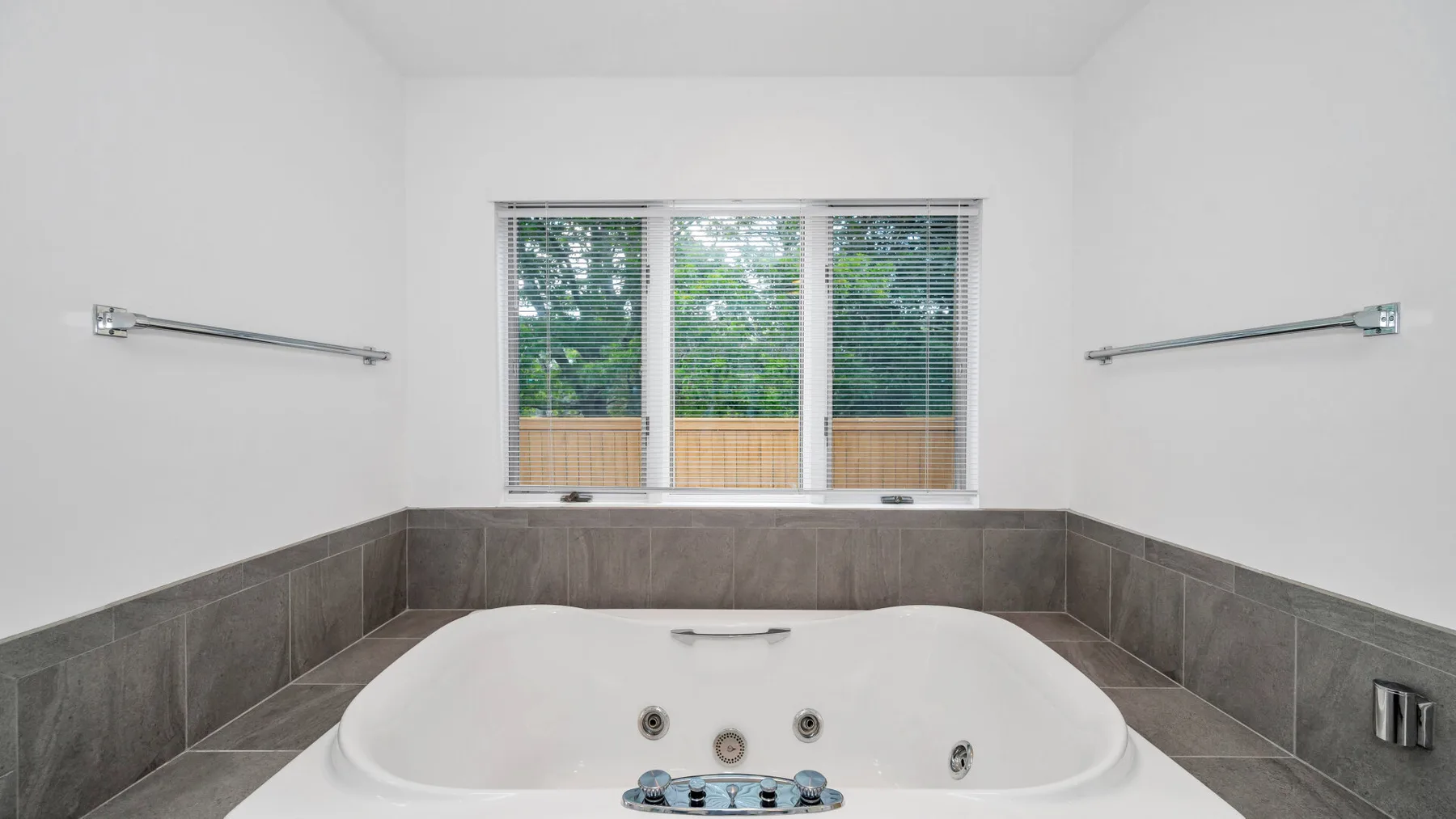 Un baño cuenta con una bañera grande bajo una ventana con persianas.