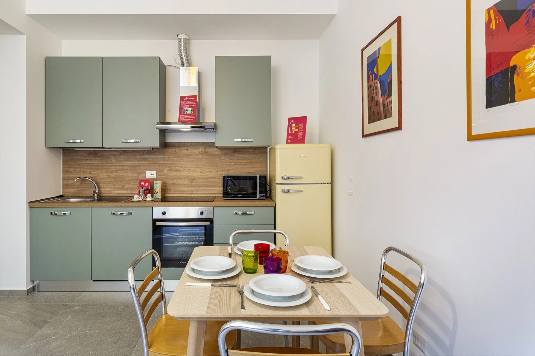 Una cocina compacta y zona de comedor con gabinetes verdes y una mesa preparada para comer.