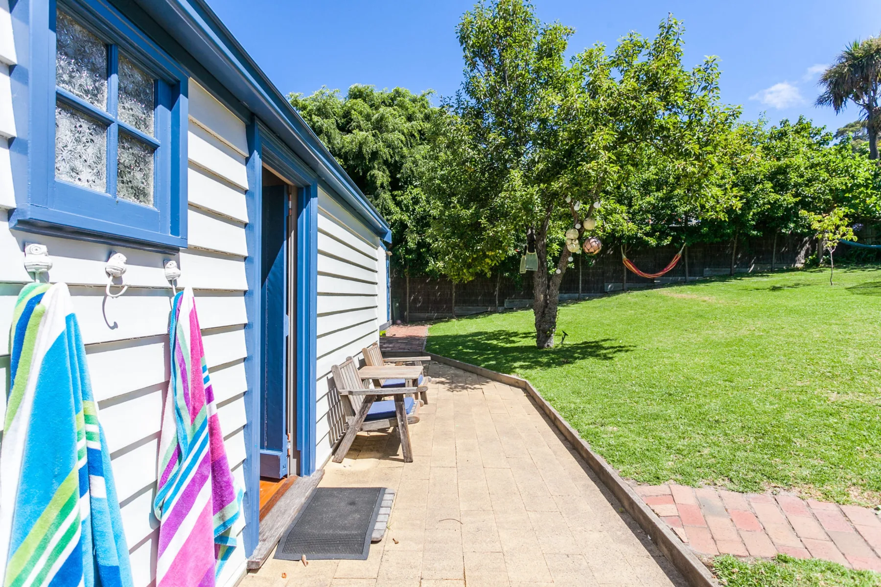 Un patio soleado junto a una casa, con asientos al aire libre y césped verde.