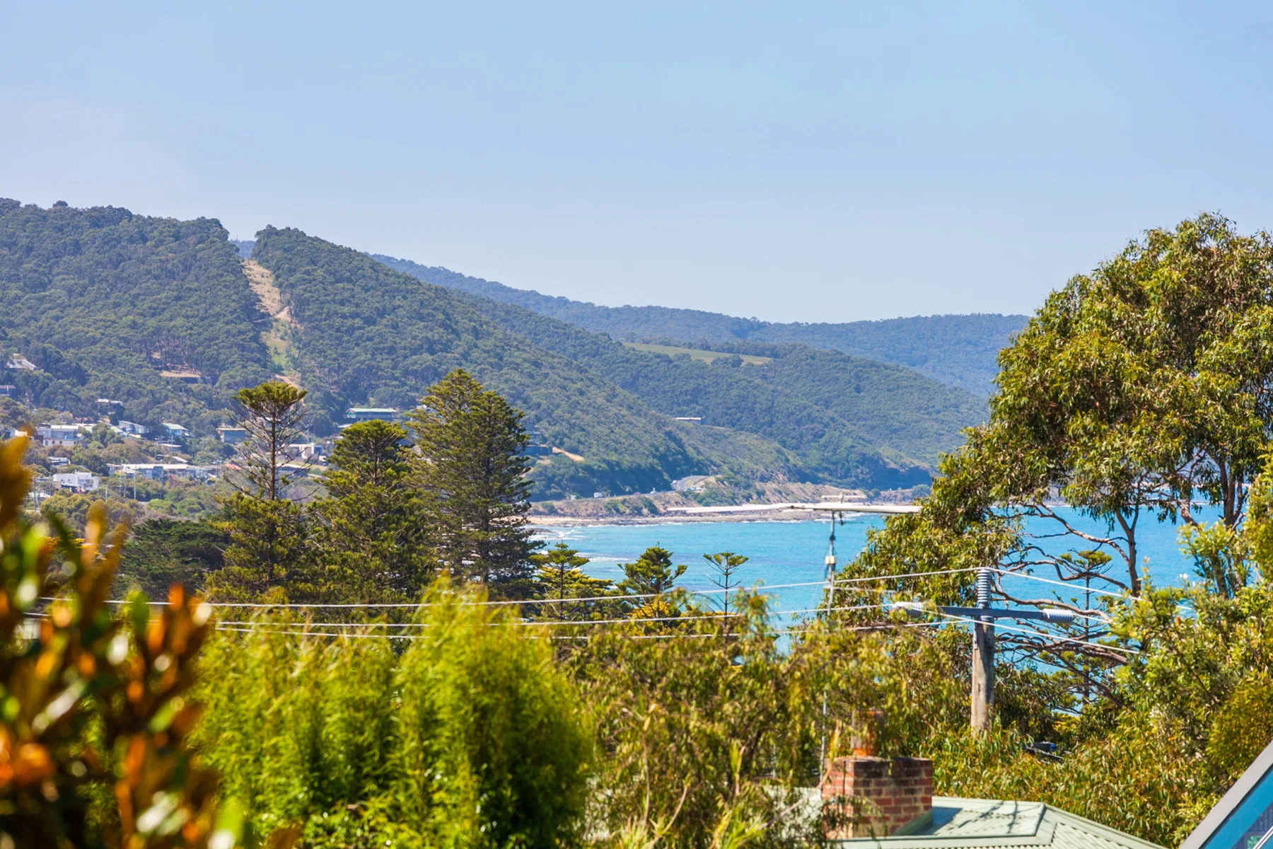 Paisaje costero con aguas turquesas, colinas verdes y árboles en primer plano.