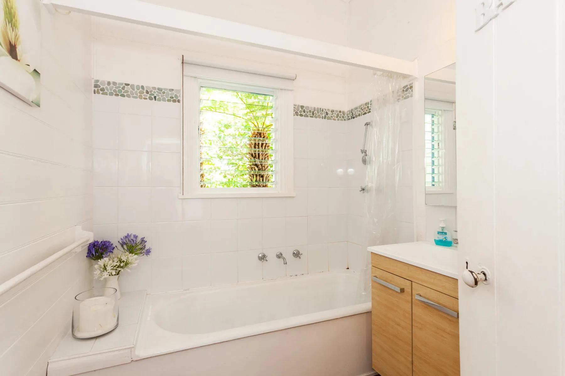 Un baño luminoso con bañera, ventana y mueble de lavabo.