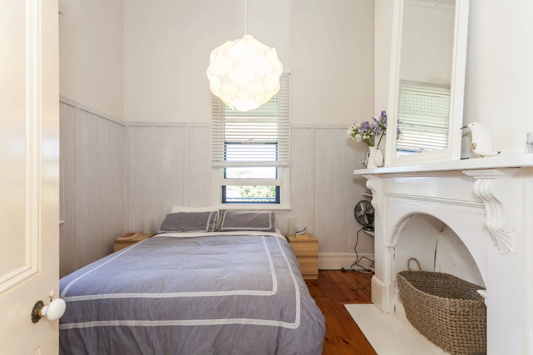 Un dormitorio con una cama bajo la ventana y una chimenea al lado.