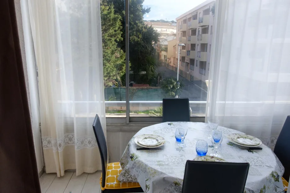 A dining table with place settings sits beside a large window with sheer curtains.