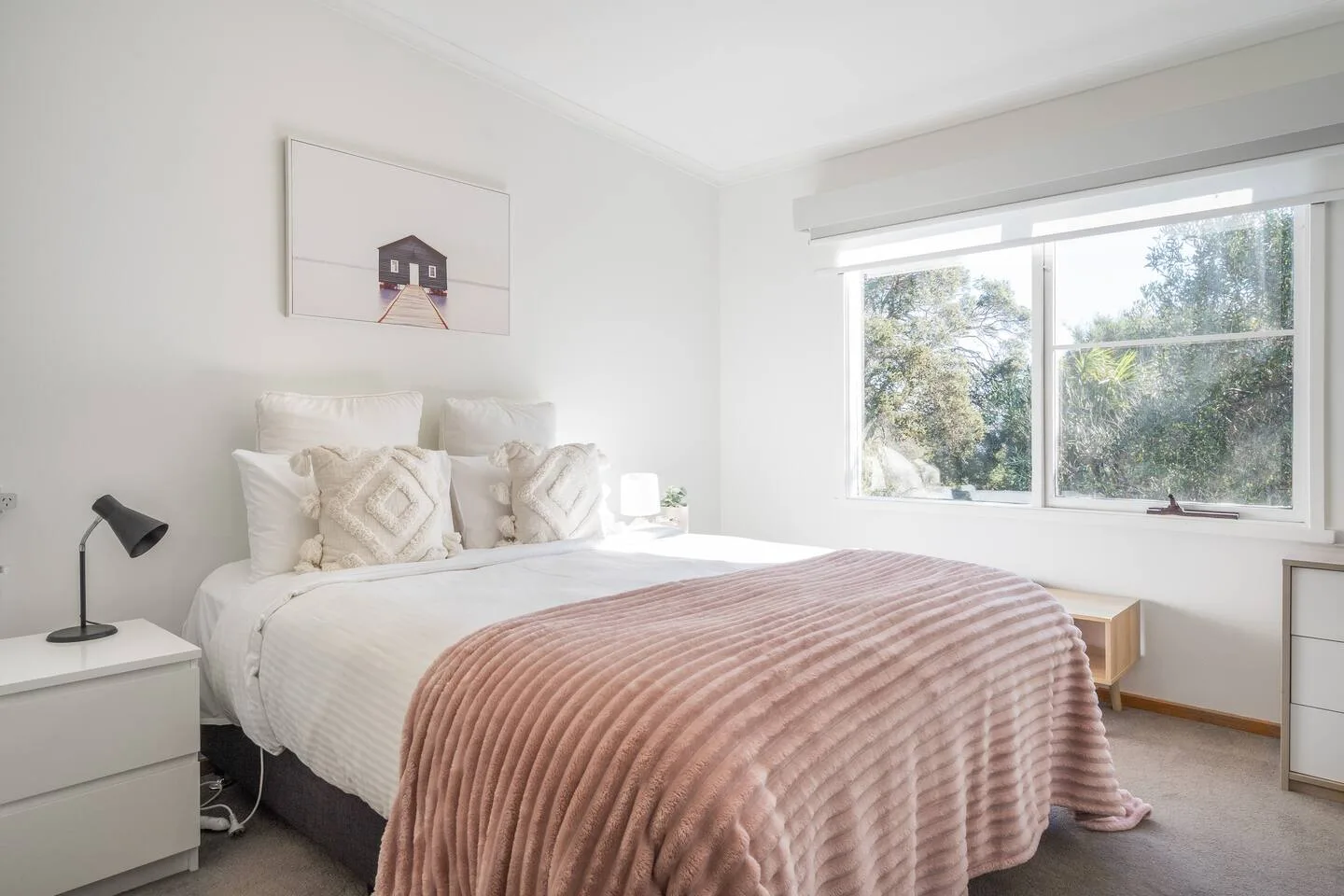Un dormitorio luminoso con una cama bien tendida y una ventana grande con vistas a los árboles.