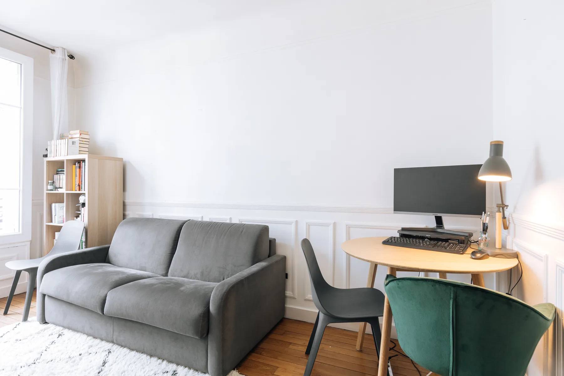 Una sala luminosa con asientos grises, un escritorio y un televisor.