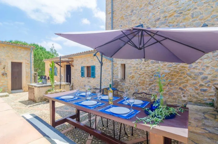 Una mesa de comedor al aire libre está bajo una sombrilla en un patio de piedra.