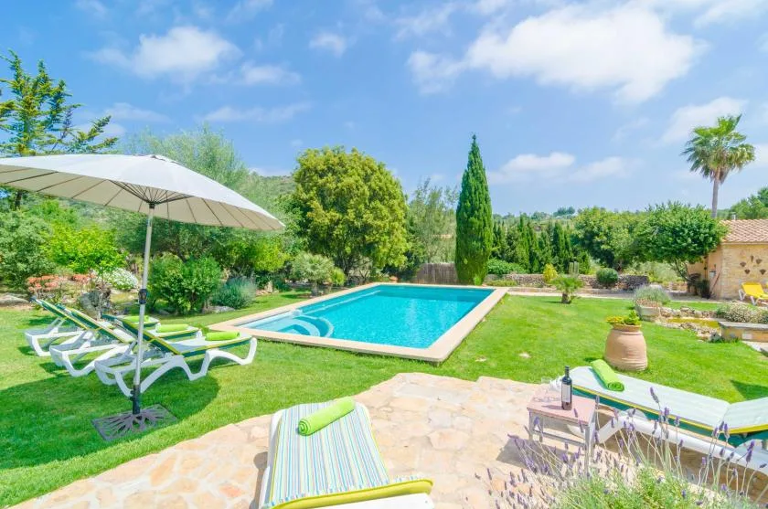 Una piscina en un jardín rodeada de césped, asientos y árboles frondosos.