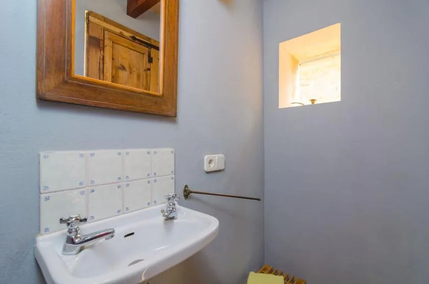 Un lavabo de baño está debajo de un espejo con marco de madera, junto a una pequeña abertura en la pared.